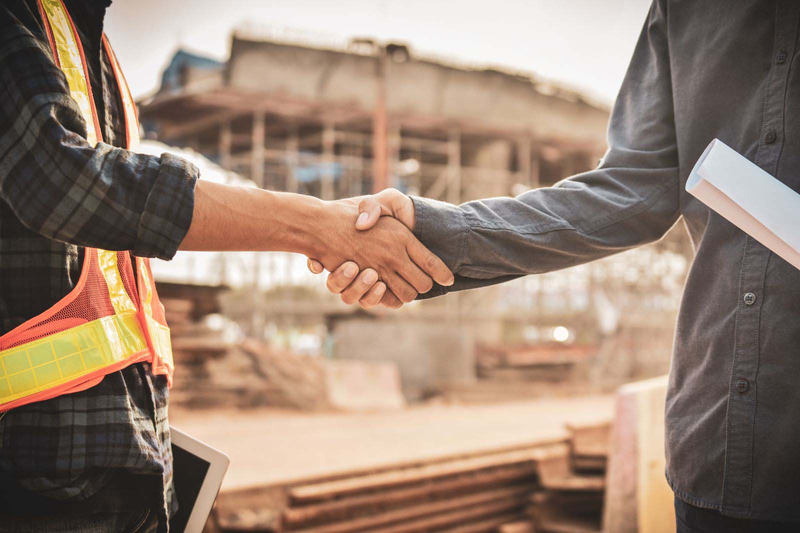 A construction worker and a foreman shaking hands in front of a workforce site